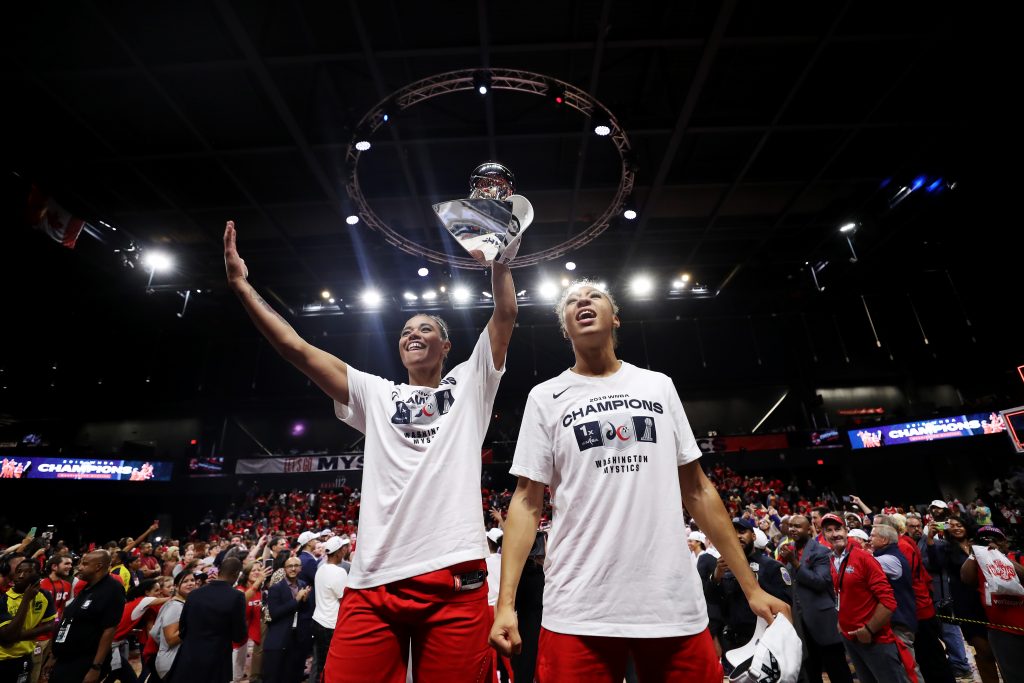 Natasha Cloud and Aerial Powers show off the WNBA Finals trophy to the crowd.